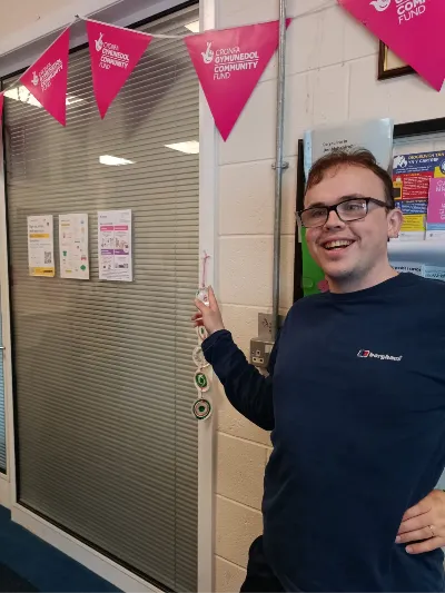 A smiling member of the Cynnig team beside a doorway decorated with bunting